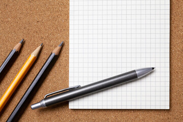 Squared notebook, pencils, pen on a cork board. The concept is back to school or office. Copy space.