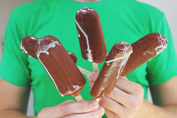 A young  caucasian man holds in his hands five pieces of ice cream on a stick in chocolate icing....