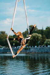 Child girl aerialist performs gymnastic split on hanging aerial silk .