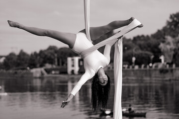 Woman aerialist performs gymnastic split on hanging aerial silk.