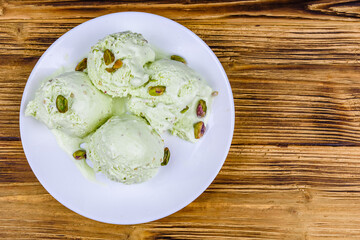 Glass bowl with pistachio ice cream balls and nuts on a wooden table. Top view