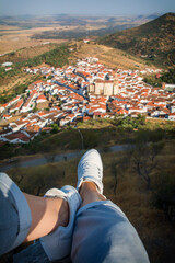 Point of view of a hiker in white sneakers overlooking a picturesque town with white houses in a mountain valley.
Hiker relaxing overlooking a city in Extremadura, Spain.