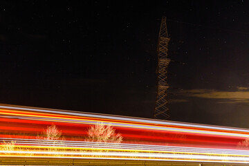 High voltage power line in a field at night. Star sky on a background. Light trails on foreground
