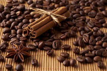 Roasted whole coffee beans, tied sticks of cinnamon and anise on a bamboo mat