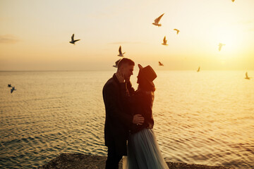 Fototapeta premium Wonderful landscape with young tourist couple at golden sunset and flying seagulls on beach. Copy space.