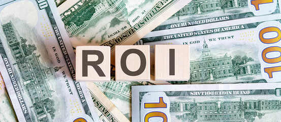 Concept words ROI on wooden blocks on a beautiful background from dollar bills.