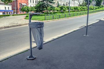 Street trash can with gray plastic garbage bag closeup on blurred cityscape background. Concept of cleanliness in tourist cities. Public utilities for garbage collection. Background with copy space