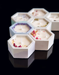 Four decorative candle with leaves of flowers in the ceramic pots in the form of honeycombs isolated on black acrylic