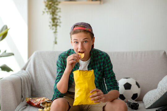 Concentrated Teen Guy Eating Chips And Watching Football Game