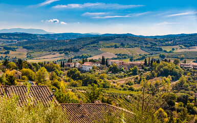 Fototapeta na wymiar Beautiful panoramic view of the lovely countryside of the famous medieval hill town San Gimignano, a typical Tuscan landscape with its valleys on a hot sunny day with a blue sky.