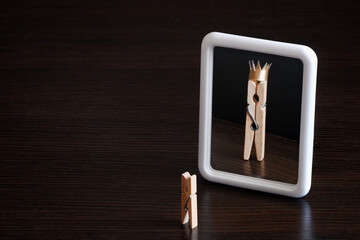 selfish concept. small clothespin seeing himself in the mirror as big king with crown
