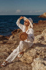 Outdoor summer fashion portrait of elegant woman wearing white linen suit, straw hat, sunglasses,...