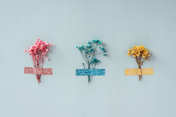 Three dry flowers glued with multi-colored tape on blue background. Pink, blue, yellow colors. Minimal design, biophilic concept for decotation.