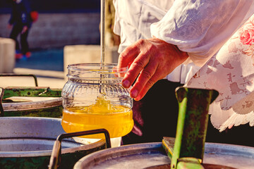 A woman puts bee honey into a plastic container using a ladle.