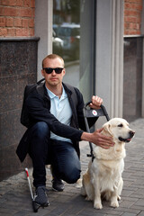 young blind man stroking guide dog in the street, caring favorite pet, best friend. outdoors