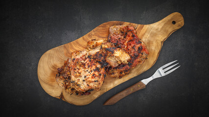 top view of tasty grilled pork with natural olive wood cutting board and fork on dark gray, grey, black tone texture background