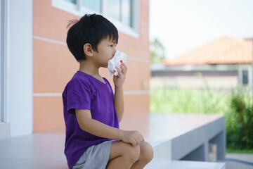 Asian boy holding blood tissue paper from nose bleeding problem