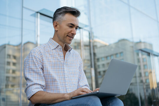 Portrait of happy programmer working project outdoors, searching on website. Handsome mature businessman using laptop computer, typing on keyboard, planning start up. Successful business concept 