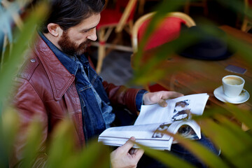 Portrait of attractive stylish man reading a magazine while drink coffee in coffee shop.