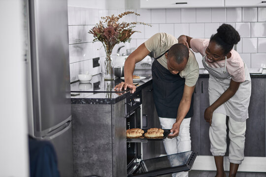 Handsome Black African Man In Aprn Open The Oven For Checking Bake. In The Kitchen