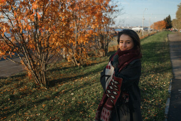 Fototapeta na wymiar Outdoor fashion photo of young beautiful lady in red scarf and dark grey coat surrounded autumn landscape.