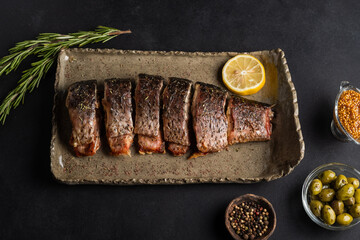 Baked carp with greens, lemon, olives and spices on a clay plate on a black background