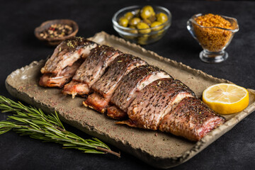 Baked carp with greens, lemon, olives and spices on a clay plate on a black background