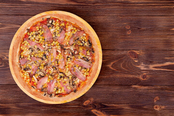 Whole pizza with chicken breast, corn, bacon and mushrooms, on a round wood plate which is on wooden rustic table, top view and copy space