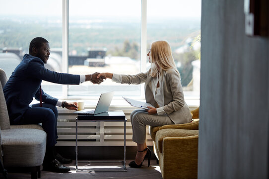 two business people shaking hands, diverse man and woman agreed with each other, they use laptop during business meeting in restaurant