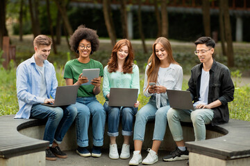 Modern Gadgets For Study. College Students Sitting Outdoors With Different Electronic Devices