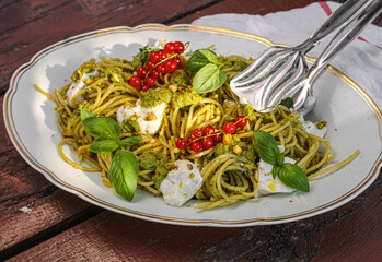 Pistachio Pesto Spaghetti topped with ricotta. Horizontal photo. Vintage silver serving tongs on the side. 
