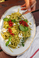 Pistachio Pesto Spaghetti topped with ricotta and red currant.  Male hand with a fork eating the pasta. 