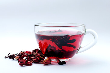 Closeup of glass cup of natural hibiscus tea and dried petals on th wt backgrund