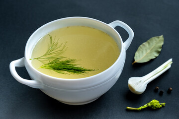 Homemade broth of meat bones in a tureen, vegetables and seasonings, on a black background. Healthy food concept.