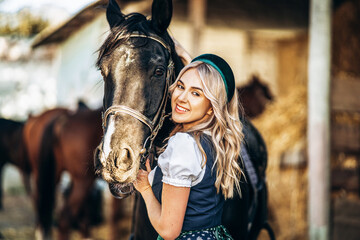 Pretty blonde in traditional dress  take care of big black horse at the farm