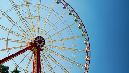 Obraz premium high ferris wheel with cabins against the blue sky. bright attraction in an amusement park on a clear blue sky on a sunny day. family vacation concept