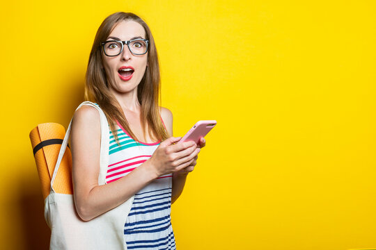 Surprised shocked young woman karimat in a bag holding a phone on a yellow background.
