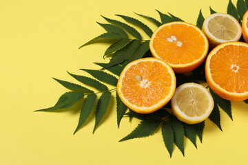 Composition of halves of lemons and oranges with green leaves on a bright yellow background