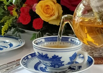 A tea kettle poured boiling water over the cup placed on the table background flowers