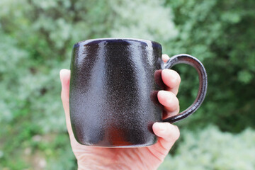 black mug made of clay. decor - covering with black engobe and transparent glaze. two firing. made on a potter's wheel. handmade