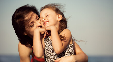 Happy beautiful mother hugging her playful enjoying kid girl on vacation sea summer holidays. Closeup outdoor