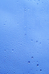Autumn window with the texture of water drops against a cloudy blue sky. Glass background with drops of rain.