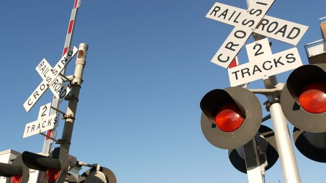 Level crossing warning signal in USA. Crossbuck notice and red traffic light on rail road intersection in California. Railway transportation safety symbol. Caution sign about hazard and train track.