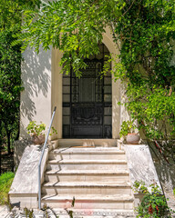 classic design house facade with marble stairs, iron and glass entrance door, plenty of foliage