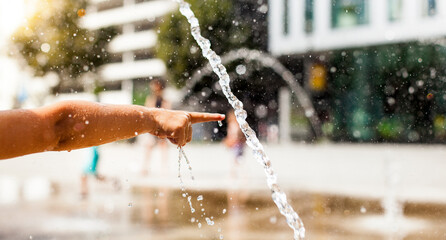 Child playing with water in the city. Cooling off in urban areas for residents. Architecture of the...