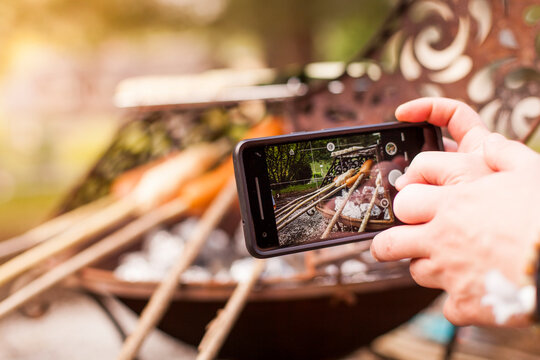 Photographing grilled sausage on a stick. Share photo with friends of the barbecue around the campfire on social media. Grillen mit Freunden am Lagerfeuer in Sozialen Medien teilen.