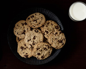 Black dish full of Home made chocolate cookies top view with a grass of milk