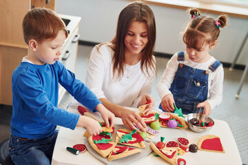 Young woman with little boy and girl playing with toys together on the kitchen