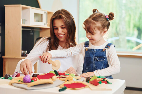 Young woman with little girl playing with toys together on the kitchen