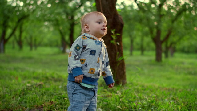 Cute Kid Boy Falling On Ground Outdoors. Little Baby Standing In Green Park.